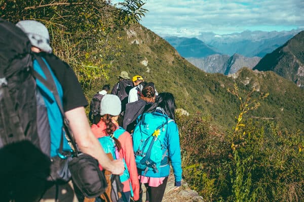People in brightly-colored backpacks hiking a mountain trail.