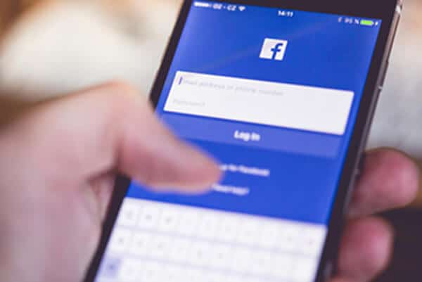 Picture of person signing into Facebook from a mobile phone. You can access Space-A flight schedules on Facebook.
