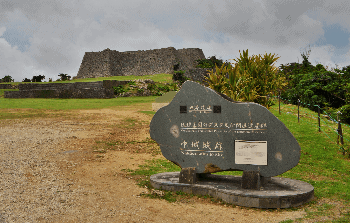 A stone entry sign with castle ruins in the background