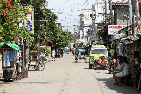 Picture of a street in Calbayog city with cars, bicycles, and people sitting outside shops