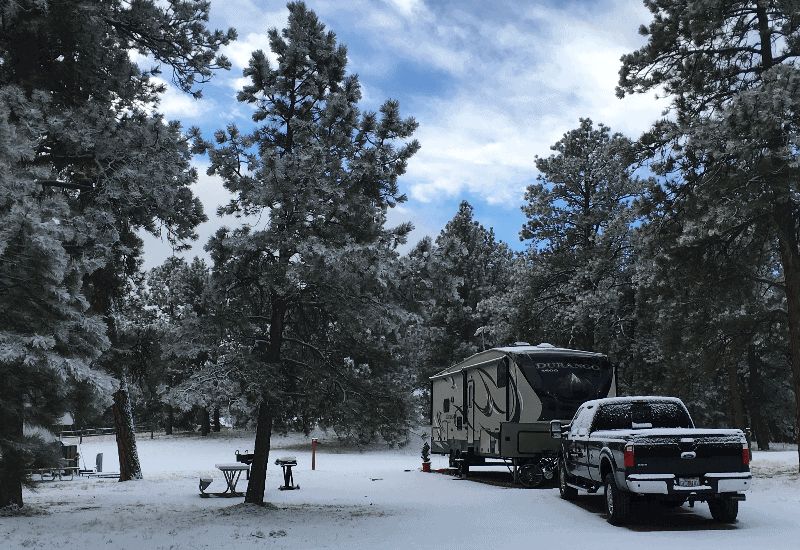 A truck behind a camping trailer in snowy woods