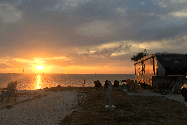 Picture of a sunset over the water with an RV parked nearby