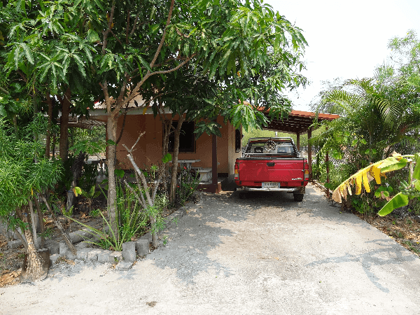 Picture of a red pick-up truck parked outside a small house in Thailand