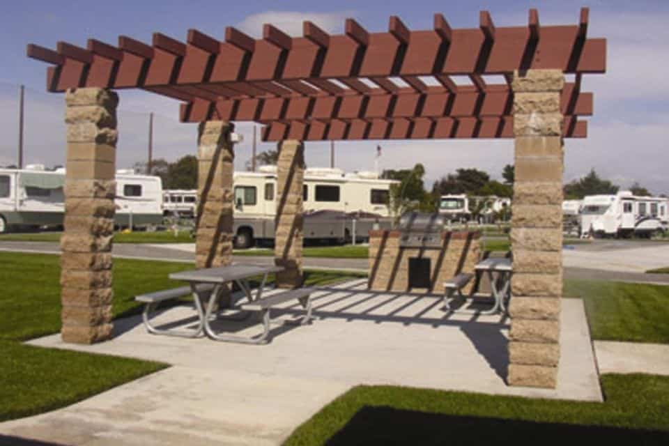 Picnic tables and a bbq grill with RVs parked nearby