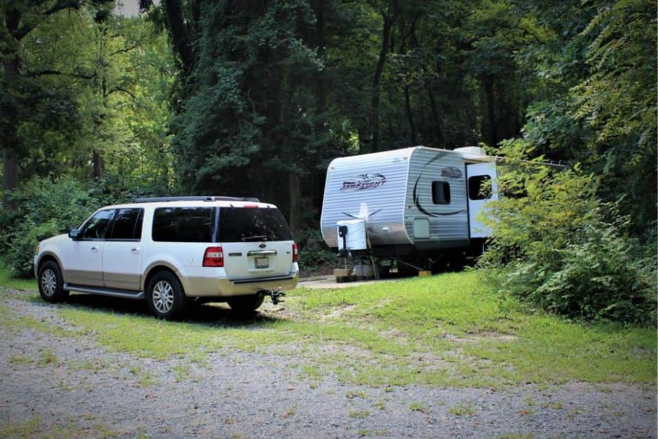 A white SUV parked next to a trailer surrounded by woode