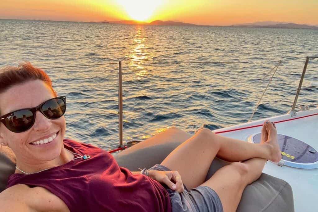 A woman on a boat taking a selfie with a sunset in the background
