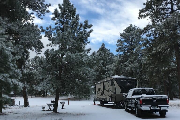 An RV hitched to a pick-up truck surrounded by snowy woods