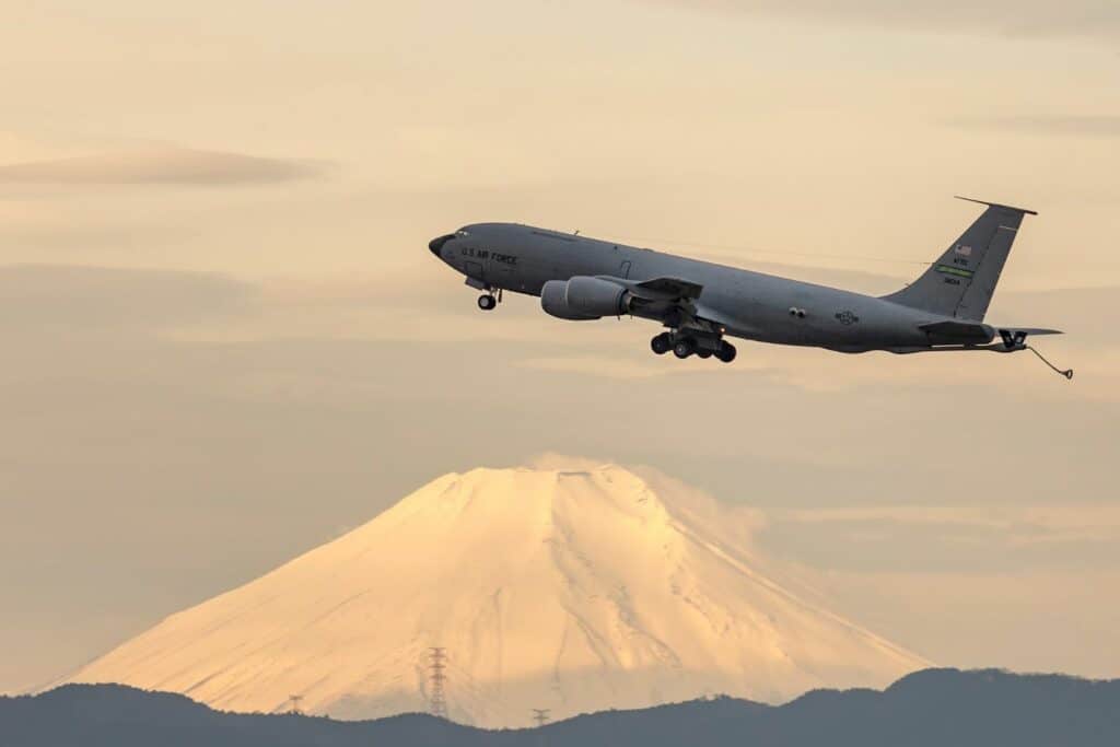 A military aircraft taking off with a snow-covered mountain in the background