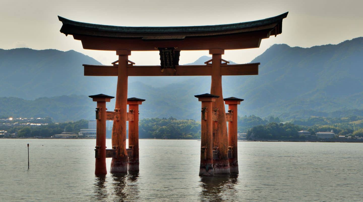 An orange Japanese shrine in water at dusk