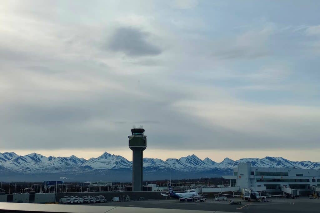 An air traffic control tower with snow-capped mountains behind it