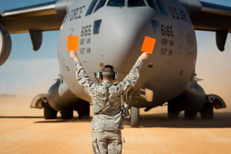An Airman stands in front of a plane holding orange flags