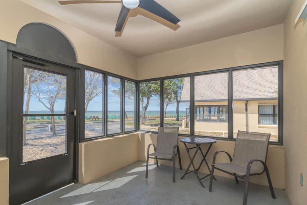 A screened patio with two chairs and table and the ocean in the background