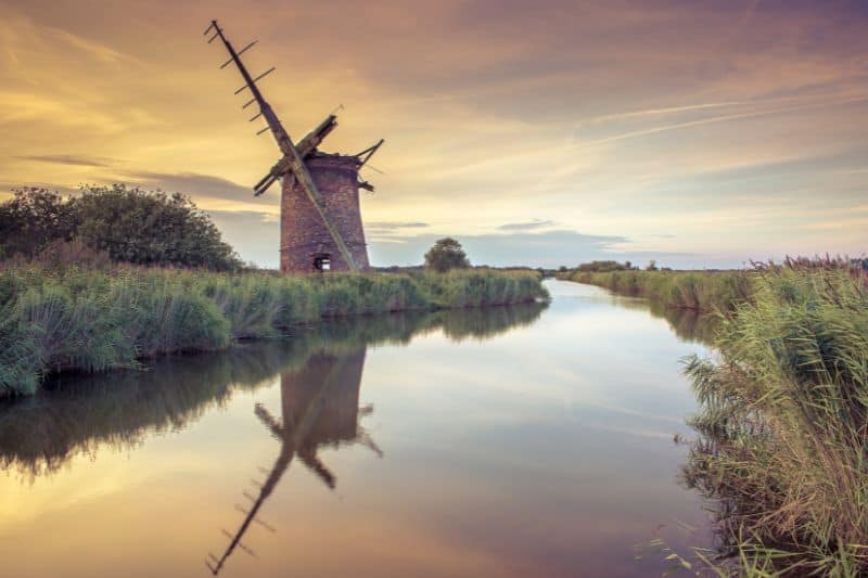 An old windmill next to a small river at sunset