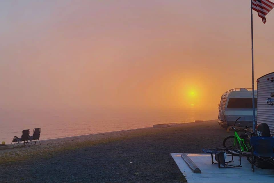 Foggy sunrise over the water with an RV parked on the shore