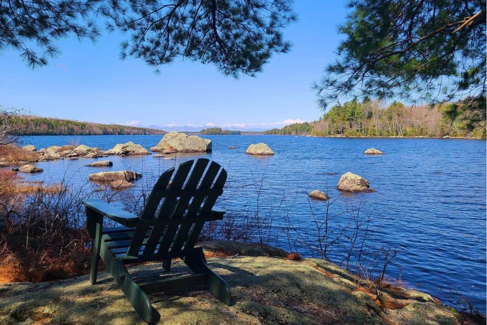 An adirondack chair next to a peaceful lake