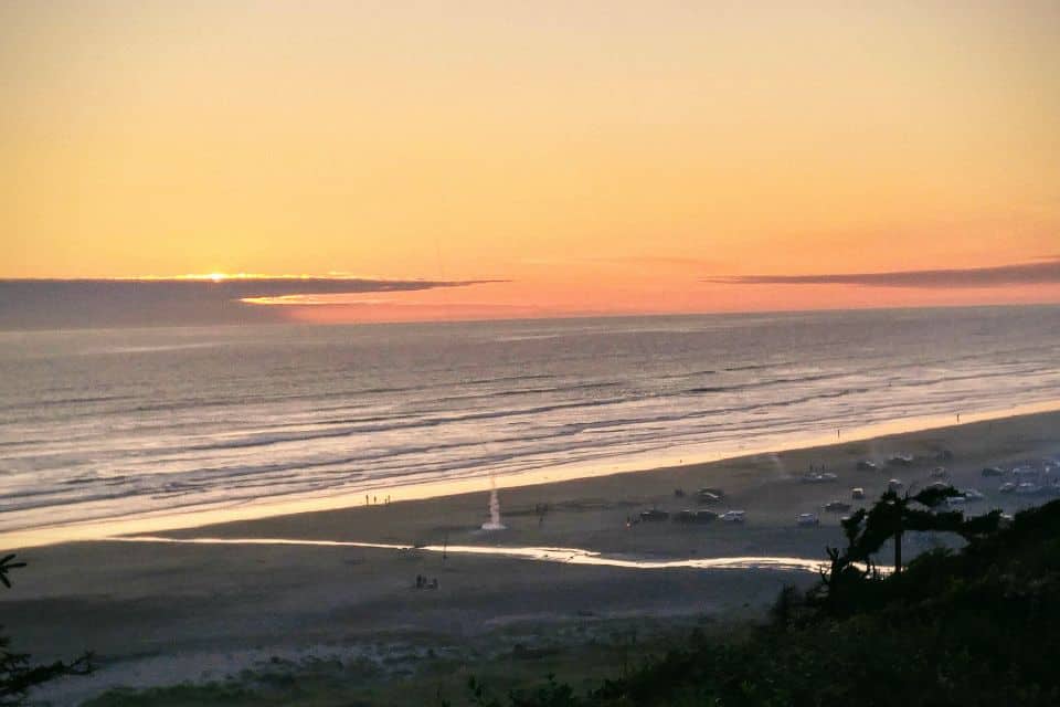 Sunset over a beach with vehicles parked on the sand