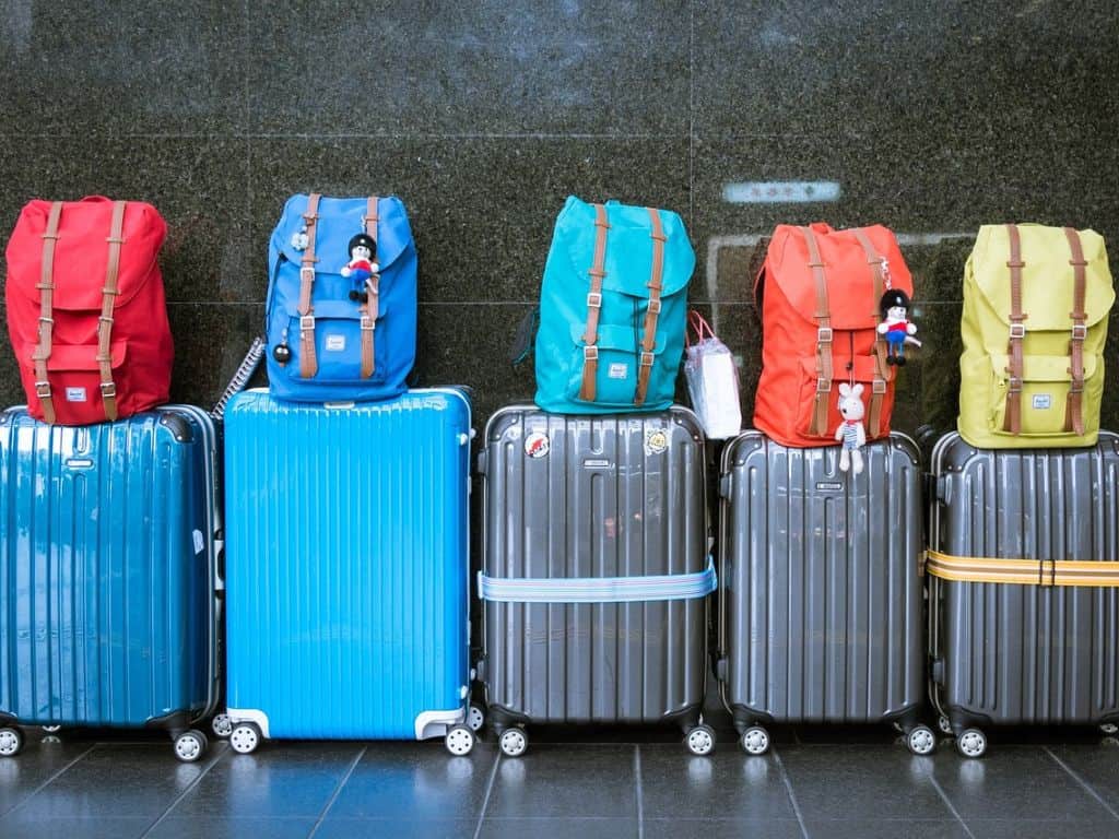 Suitcases lined up in a row with colorful backpacks on top