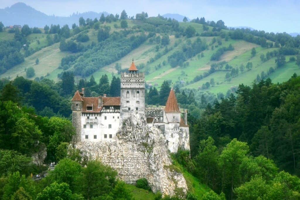 A large castle on a mountain surrrounded by greenery