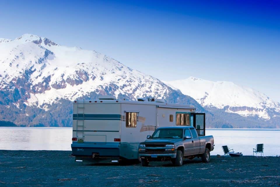 A pickup truck parked next to a trailor with snow-covered mountains in the background