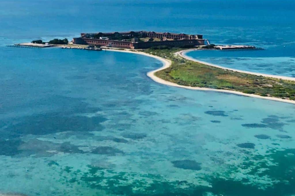 an island with a fortress surrounded by turqoise water as seen from above