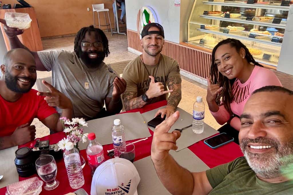 Group of veterans and friends smiling around a table at a café.