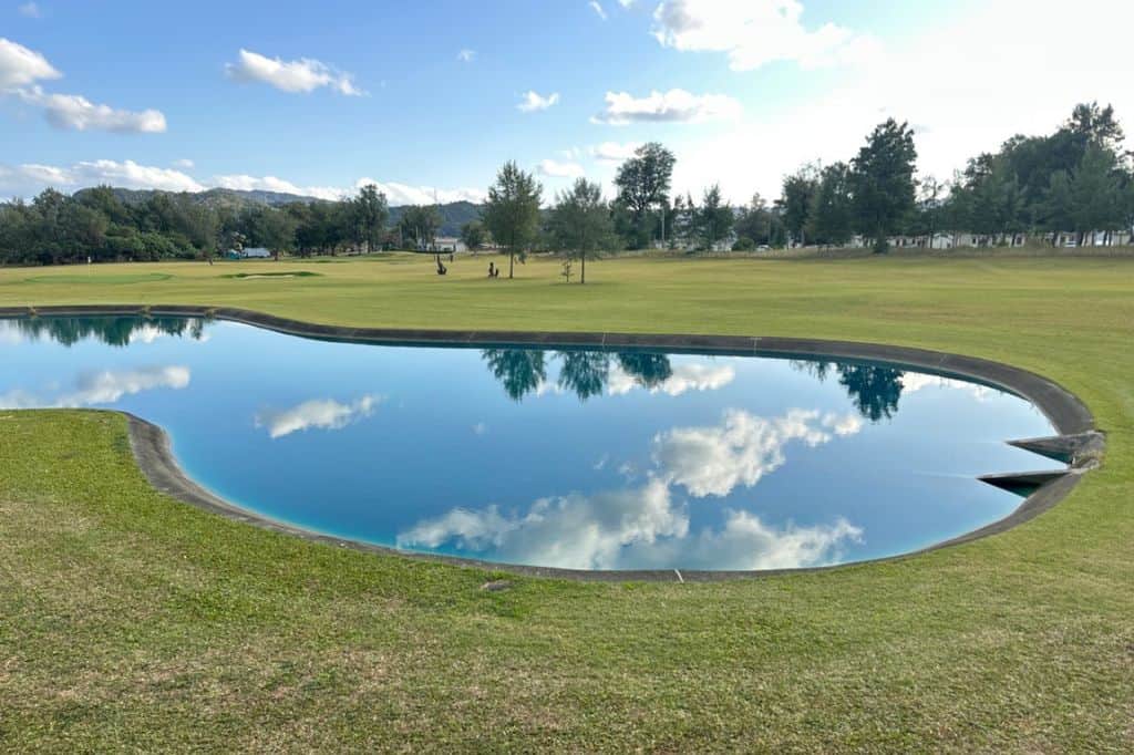 A golf course with a pond reflecting the sky