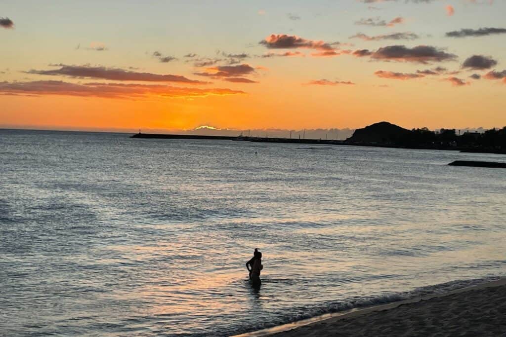Vibrant orange sunset over Waianae Harbor on Oahu, with a silhouette of a person standing in the water.