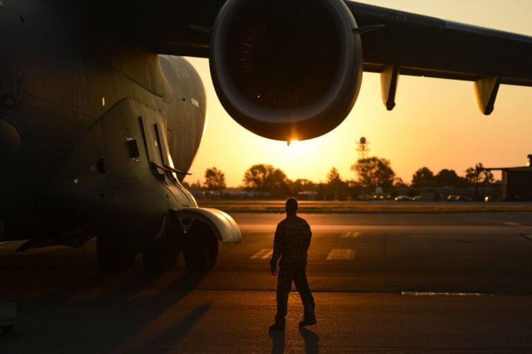 A service member stands beside a C-17 cargo plane at dawn