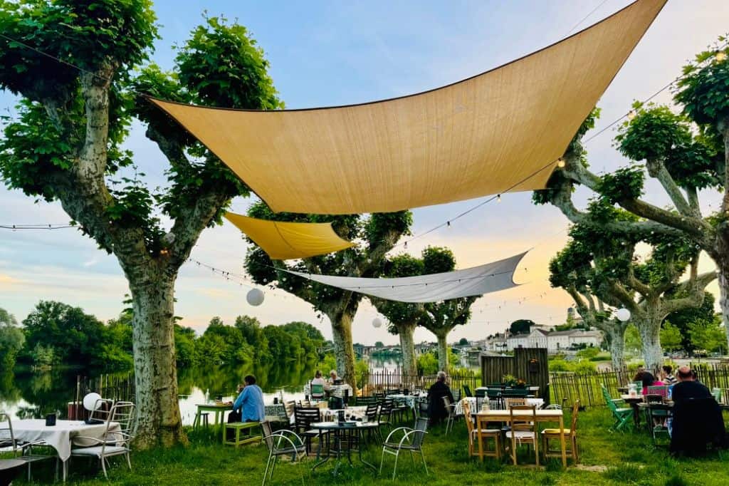 Riverside café with shade sails and diners along the Dordogne River in France
