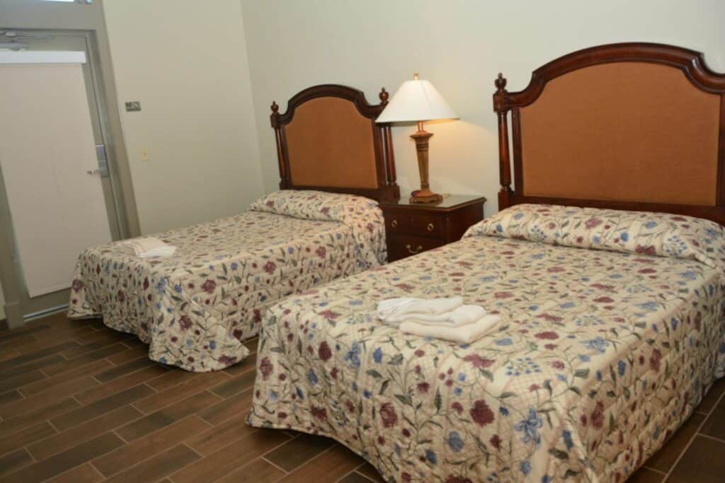 Two full-size beds in a Jackson Barracks guest room with wood floors and bedside table