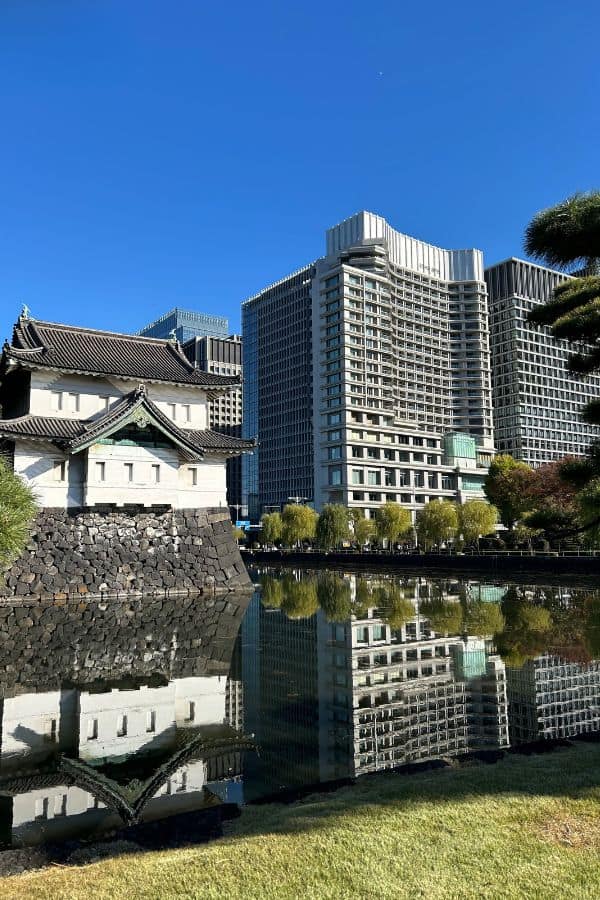 View of Tokyo’s Imperial Palace moat reflecting historic stone walls and modern skyscrapers under a clear blue sky.