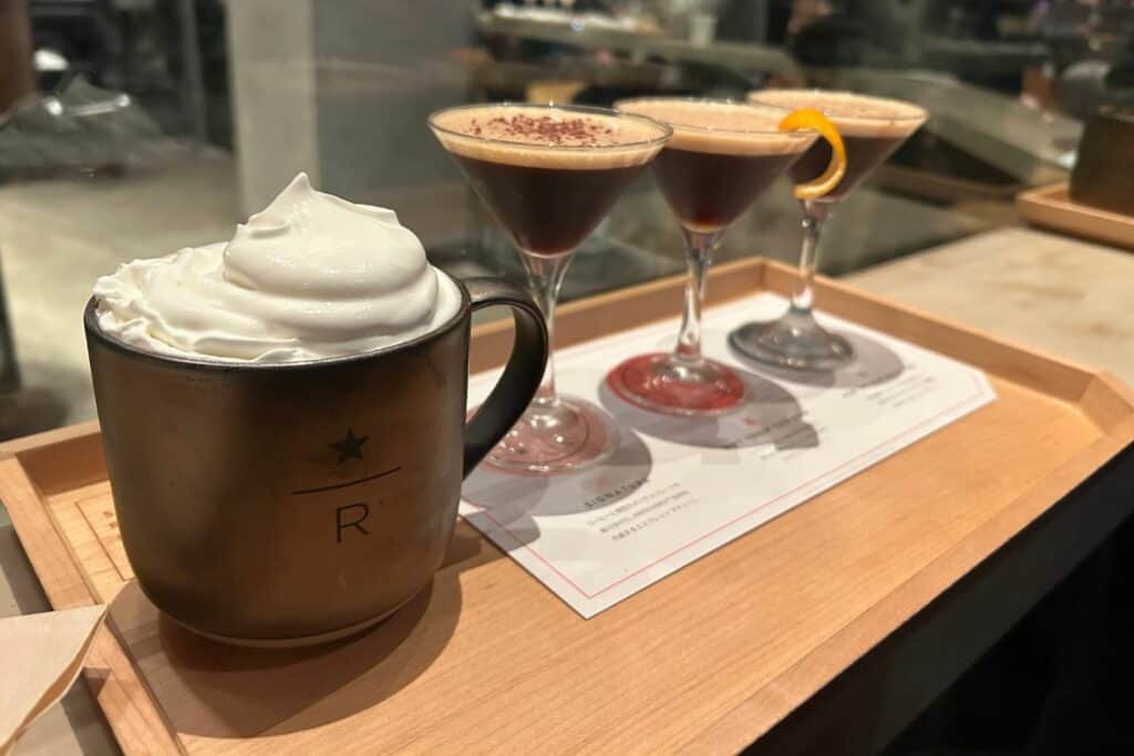 A muug of hot cocoa brimming with whipped cream and a row of martini glasses filled with espresso