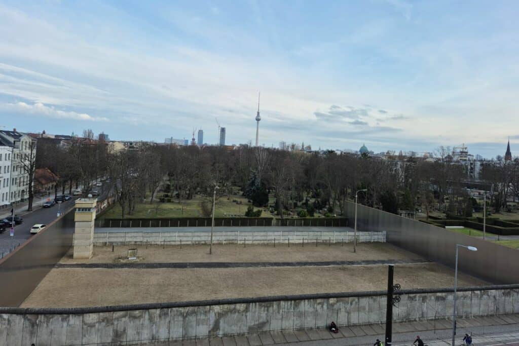 Concrete wall segment and watchtower at Berlin Wall Memorial with city skyline in the background