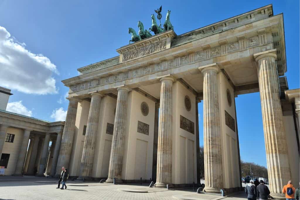 Side view of Brandenburg Gate’s columns and archways with visitors walking nearby in Berlin