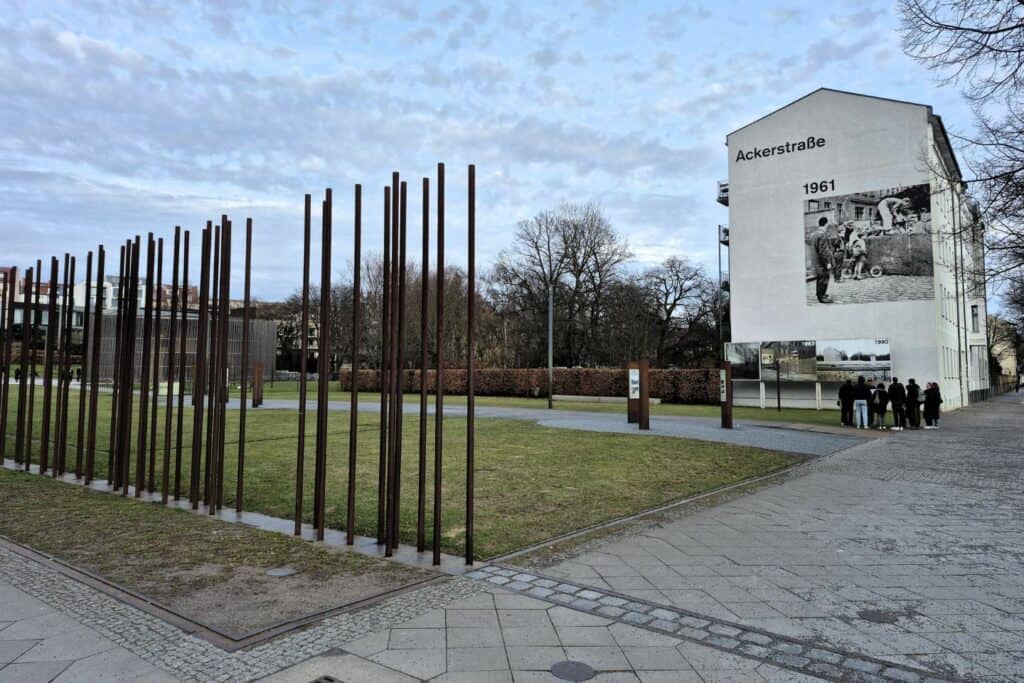 Steel poles marking the former Berlin Wall border with historic photo display on nearby building
