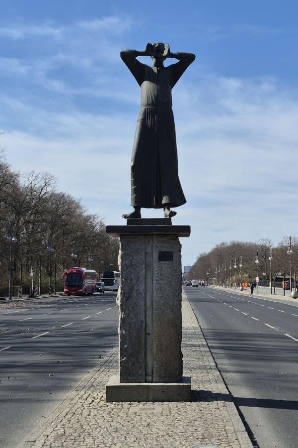 Statue of a person with hands raised to his mouth standing on a pedestal in the middle of a wide street