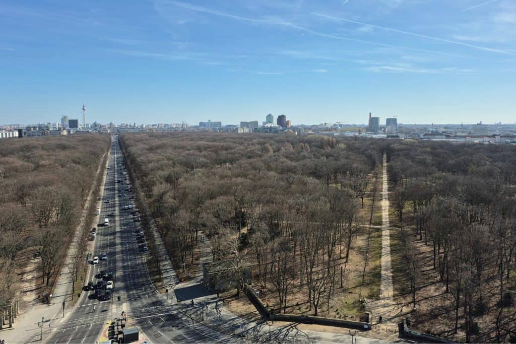 View over a large park and tree-lined paths with Berlin skyline in the distance