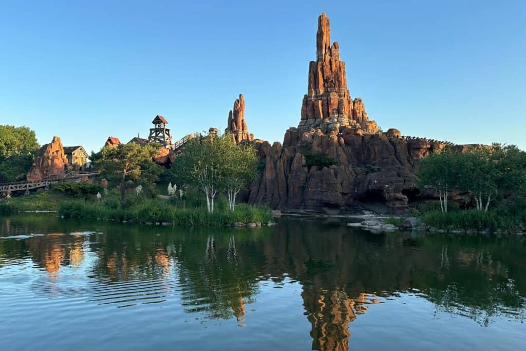 A roller coaster running through artificial rock formatrions in front of a pond
