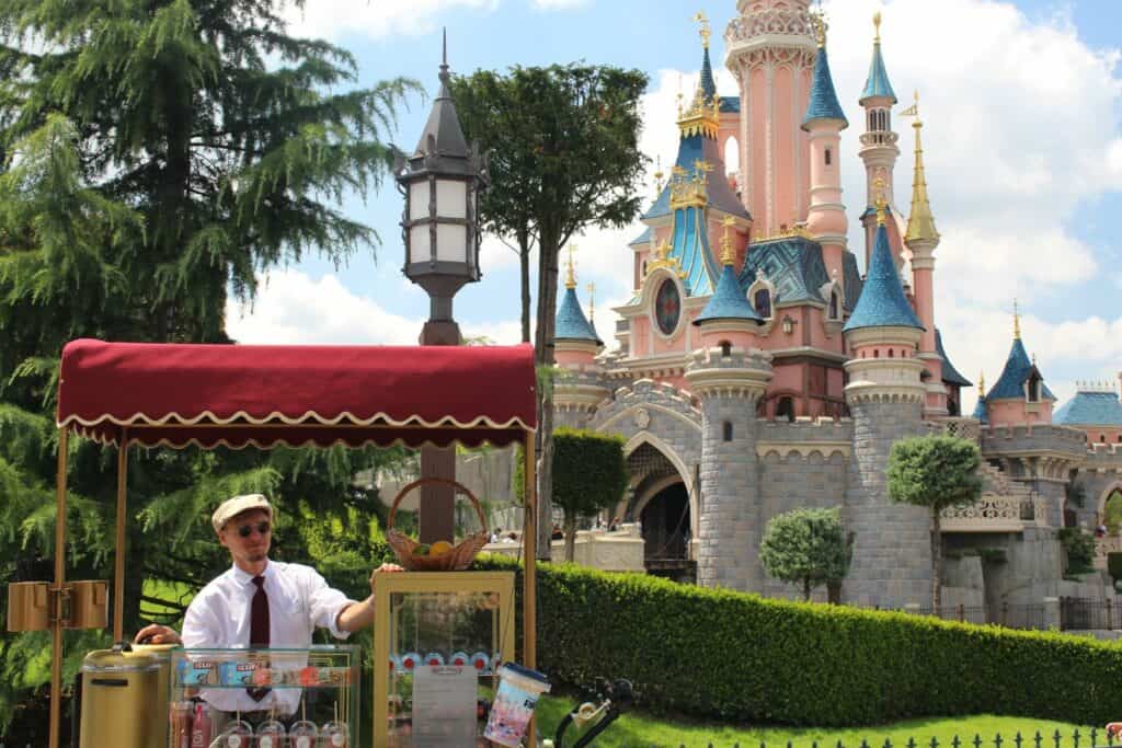A vendor wearing a beret behind a food stand with Cinderella's castle in the background