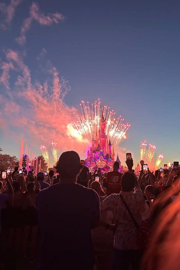 crowds watching a fireworks display over cinderella's castle at disneyland paris