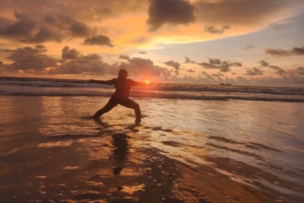 Isah practices yoga in shallow ocean water during sunset on a Costa Rica beach.