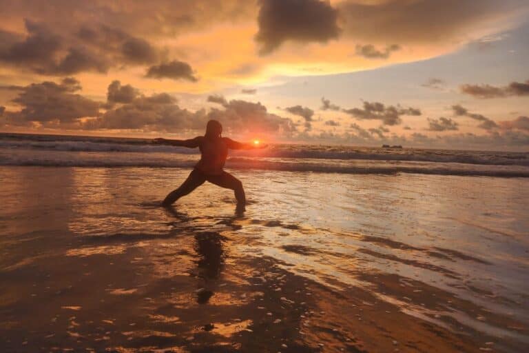 A woman practices yoga in shallow ocean water during sunset on a Costa Rica beach.