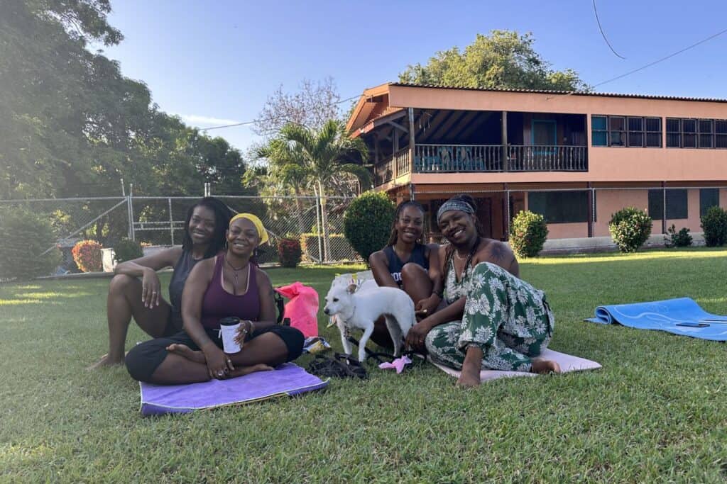 Isah sits with three women and a small white dog on yoga mats outside a building in Costa Rica.