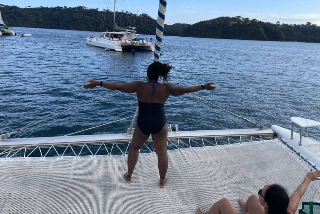 Isah stands with arms outstretched on the netting of a sailboat off the coast of Costa Rica.