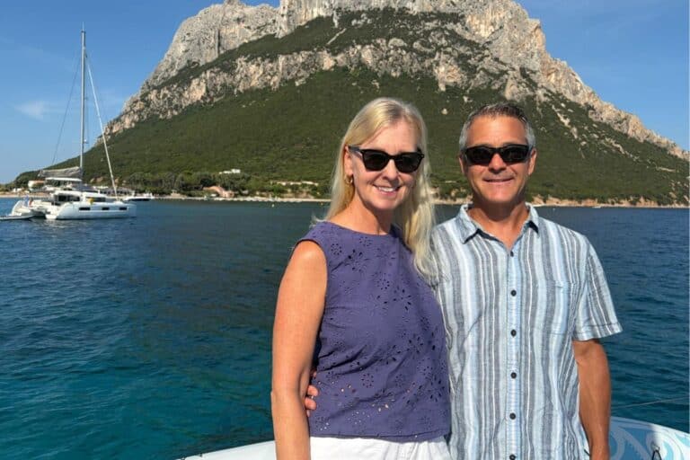 A couple standing on their boat with a mountain in the background
