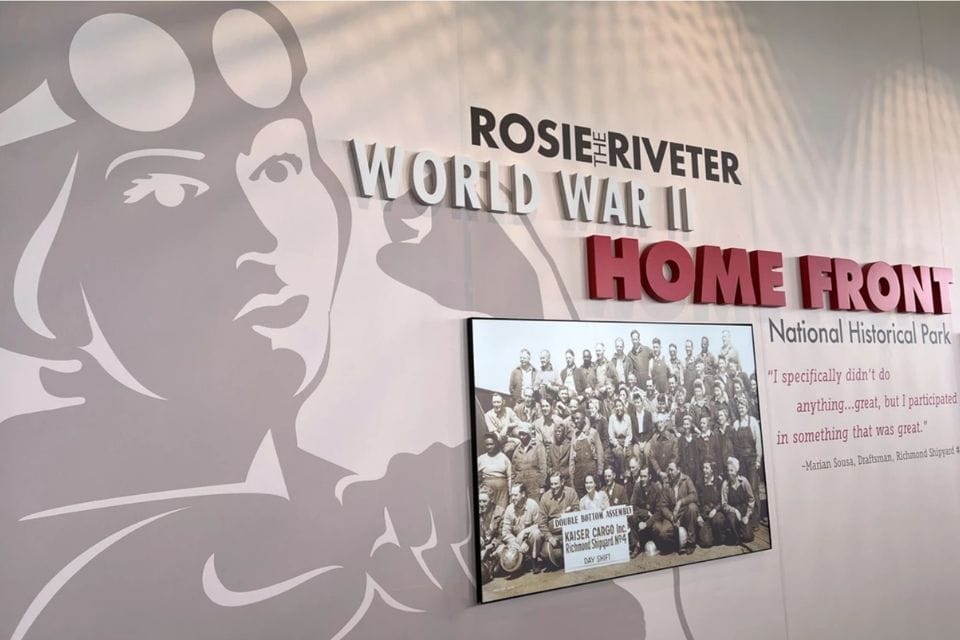 Interior exhibit wall with Rosie the Riveter artwork, World War II Home Front sign, and historic worker photo