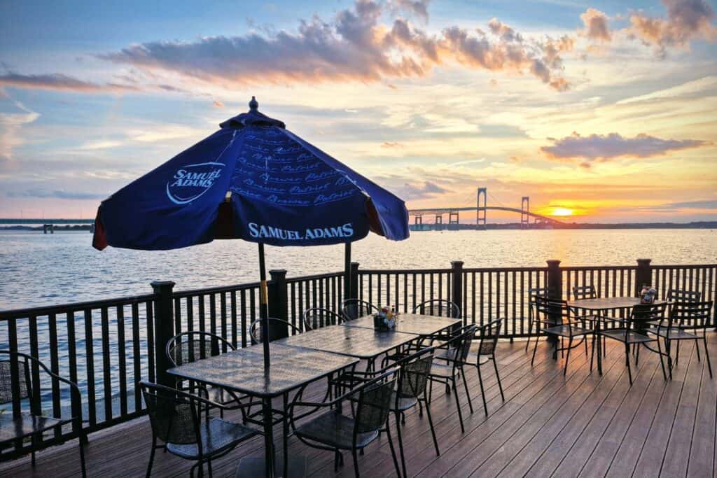 Outdoor dining tables overlooking Narragansett Bay and the Newport Bridge at sunset