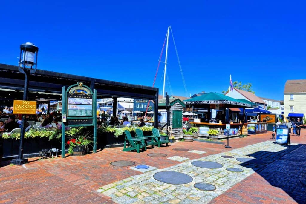 Busy Newport wharf with outdoor dining, brick walkways, shops, and a sailboat mast