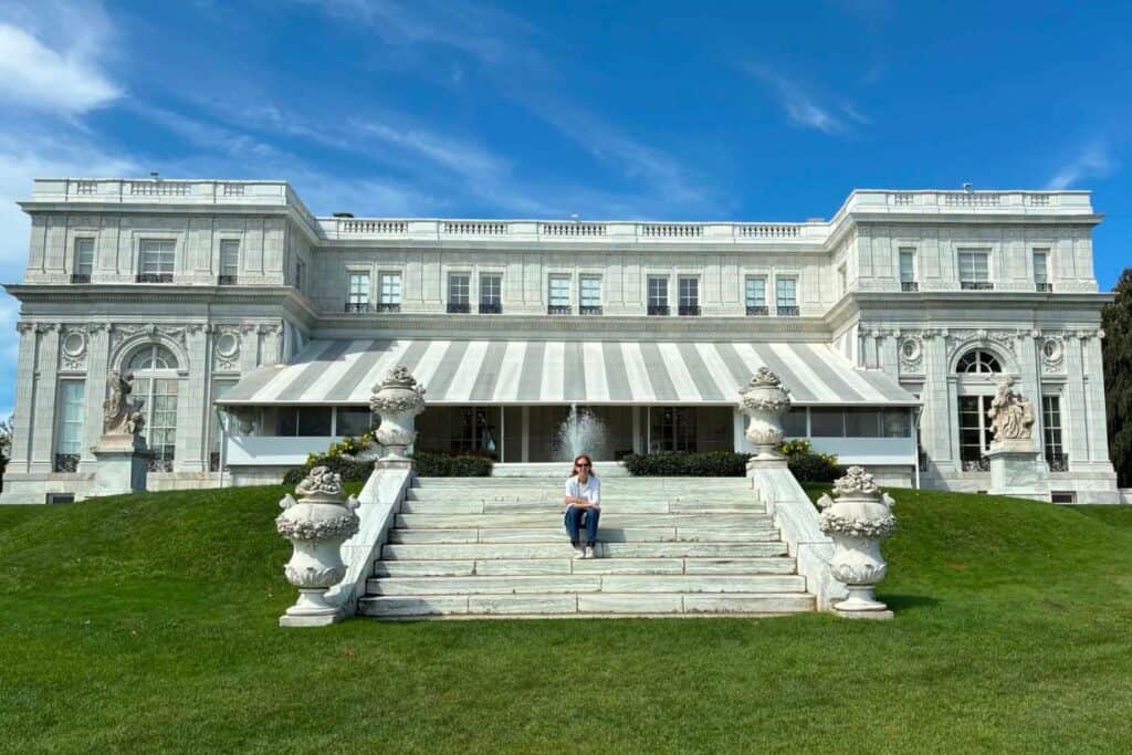Rosecliff mansion with its white stone exterior, broad lawn, and Stephanie sitting on the steps