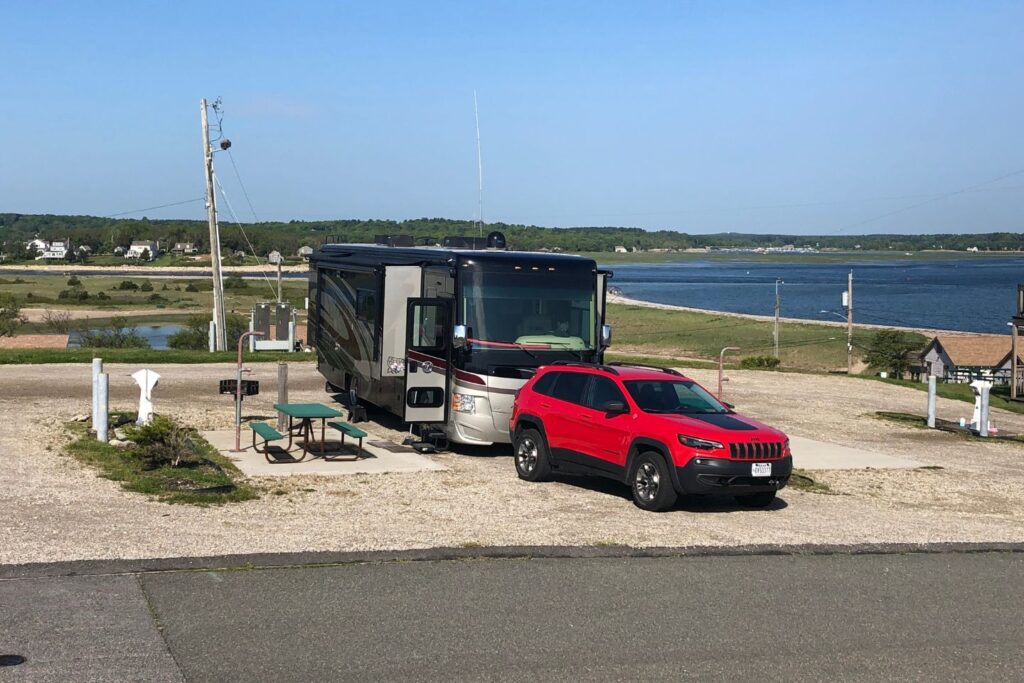 A large motorhome with a red SUV parked in front with views of the ocean in the background